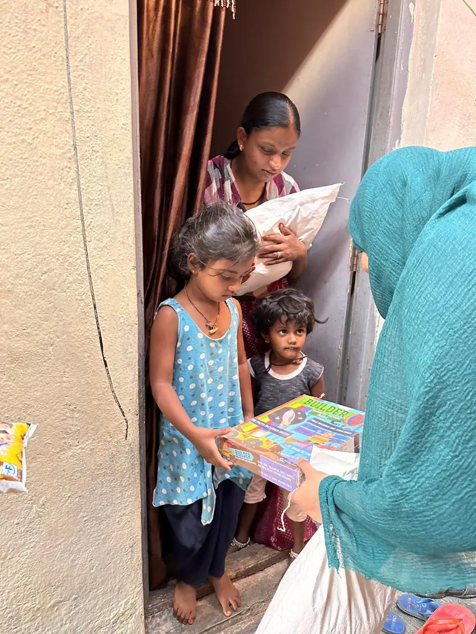 Volunteer handing school supplies to children at a doorway.