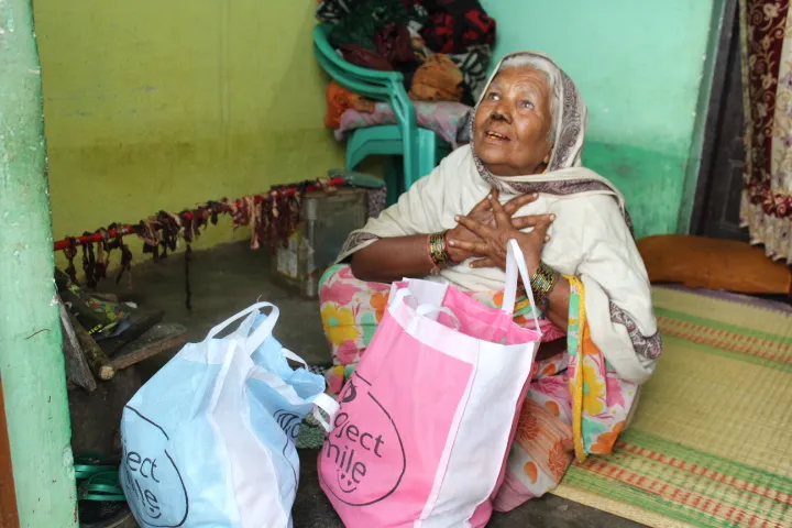 Older woman seated on a bed with a support package beside her.